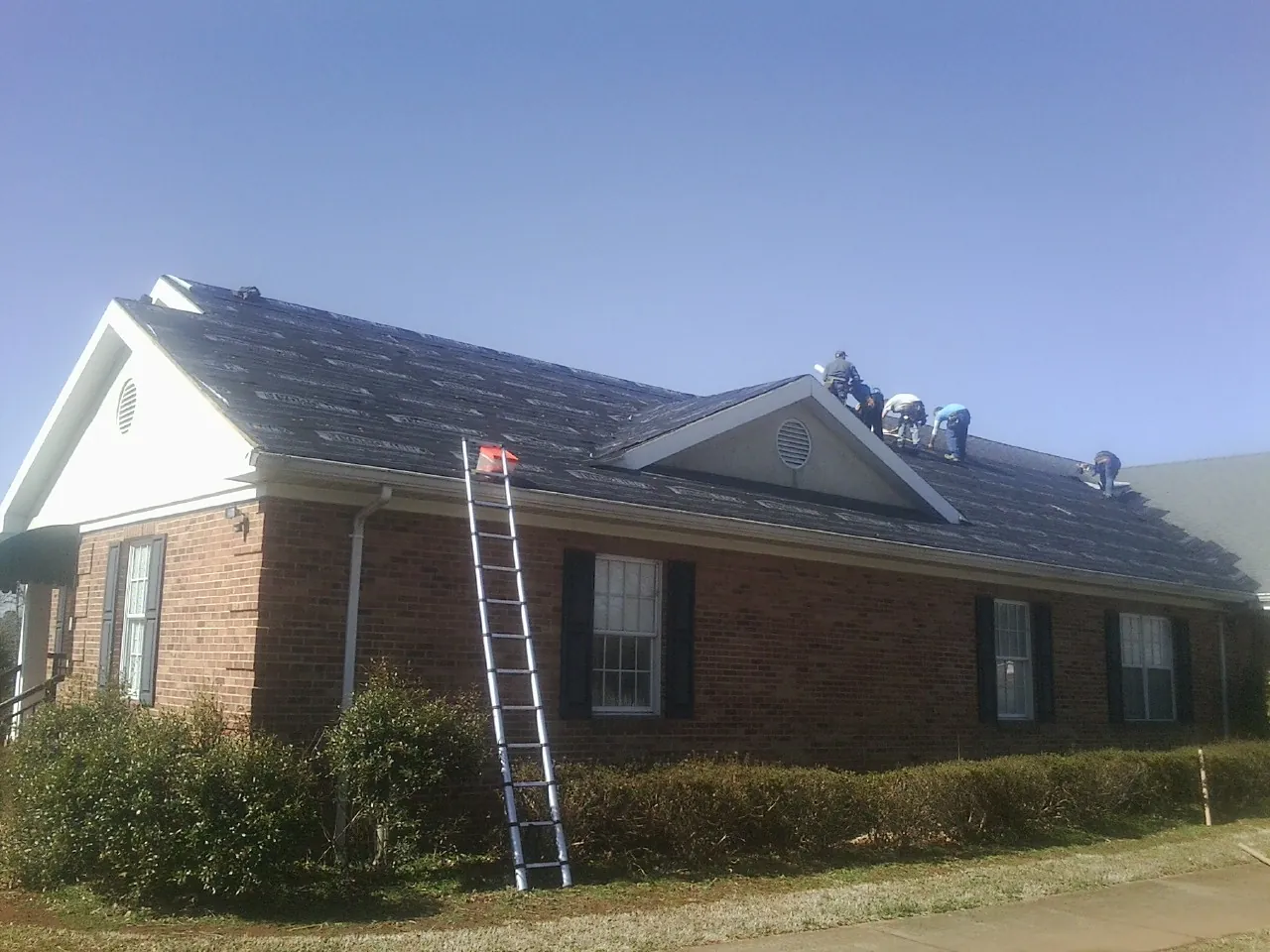 Crew tearing shingles off a brick ranch roof with a ladder set — Emergency Roof Repair work by our crew in Holland