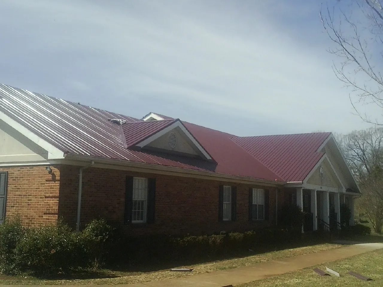 Red metal roof with gabled entries on a long brick building, from a Hail Damage Roof Repair job in Holland